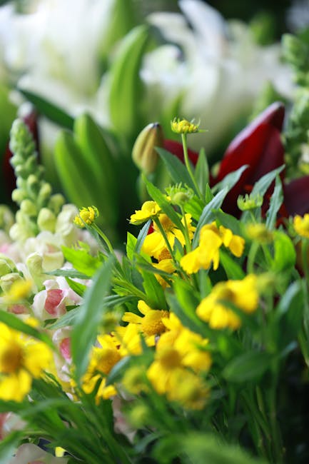 A vibrant, hand-held bouquet of fresh flowers featuring white daisies with yellow centers, bright yellow primulas, purple statice, and delicate pink and purple blossoms, arranged in a natural, loosely