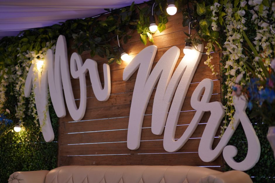 A wedding aisle adorned with abundant white floral arrangements, featuring roses and hydrangeas, arranged along the pathway and forming a large floral archway at the entrance. The flowers are fresh, w