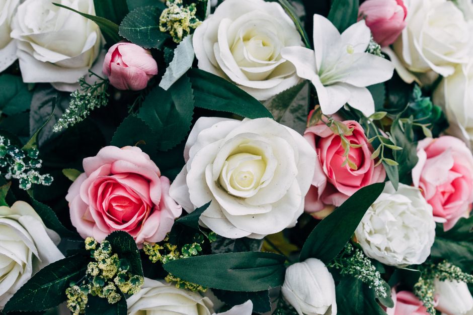 A close-up view of a large, round floral bouquet arranged with a variety of fresh roses in shades of peach, cream, blush pink, and mauve, interspersed with yellow and orange blooms, pale green hydrang