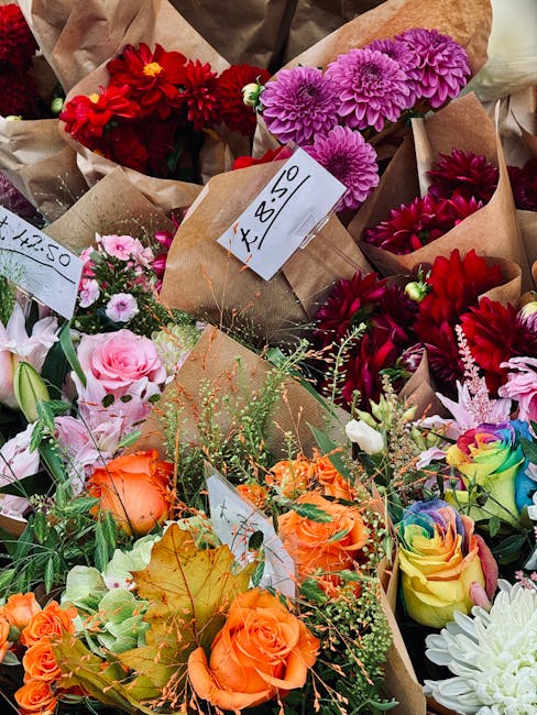 A variety of fresh flower bouquets arranged on a display table, featuring pink, purple, white, and red blossoms including lisianthus, roses, and small daisies. The flowers are wrapped in clear celloph